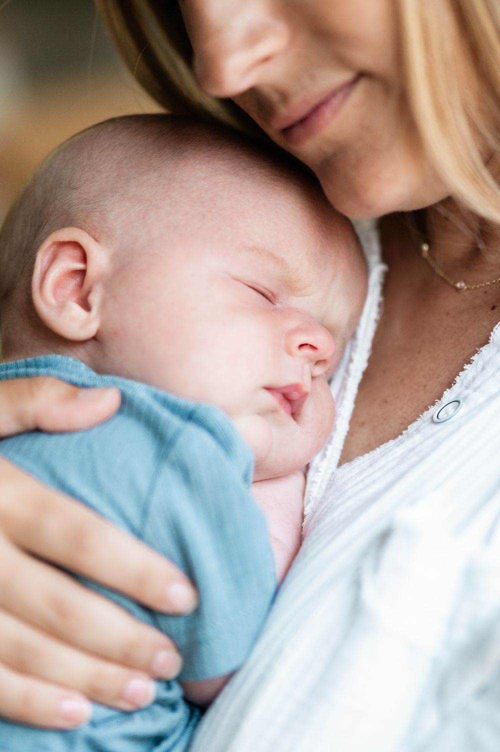 A mother tenderly holds her sleeping newborn baby wrapped in a soft blue blanket close to her chest.