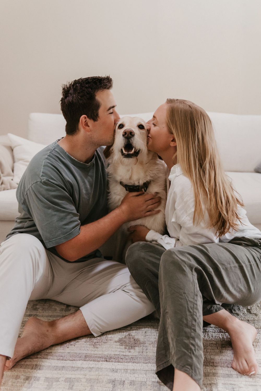 An at home couple session featuring the couple in front of their couch kissing this golden doodle dog,