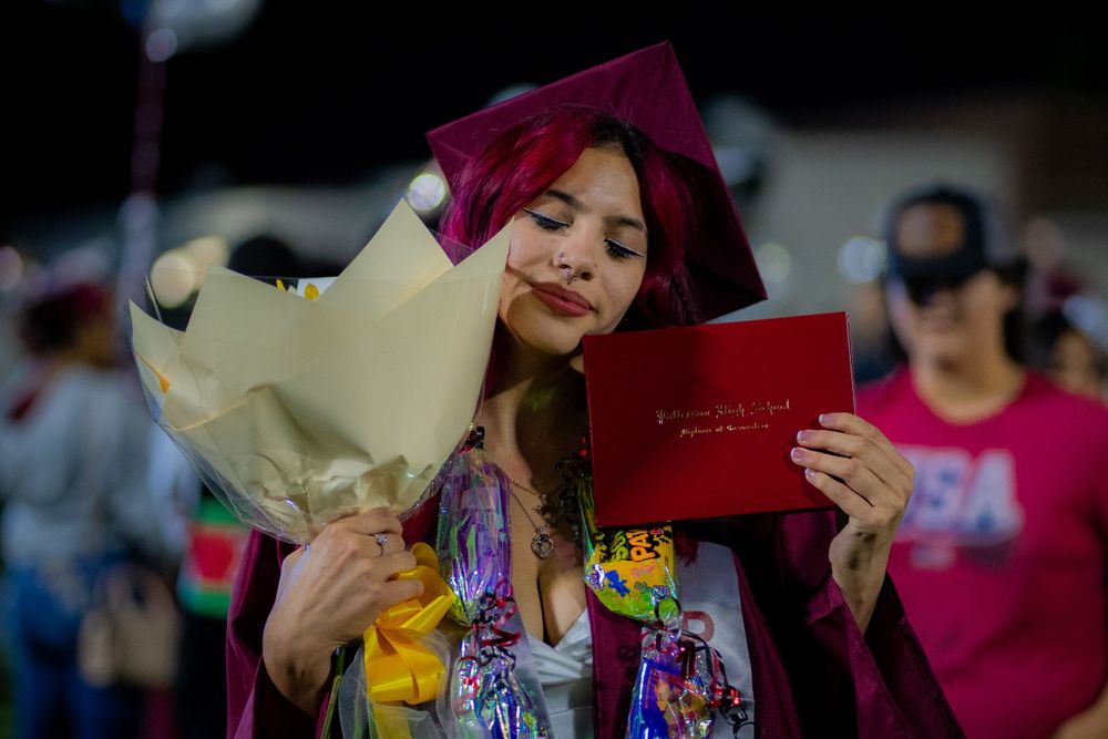 Graduate holding flowers and diploma while smiling in burgundy cap and gown.