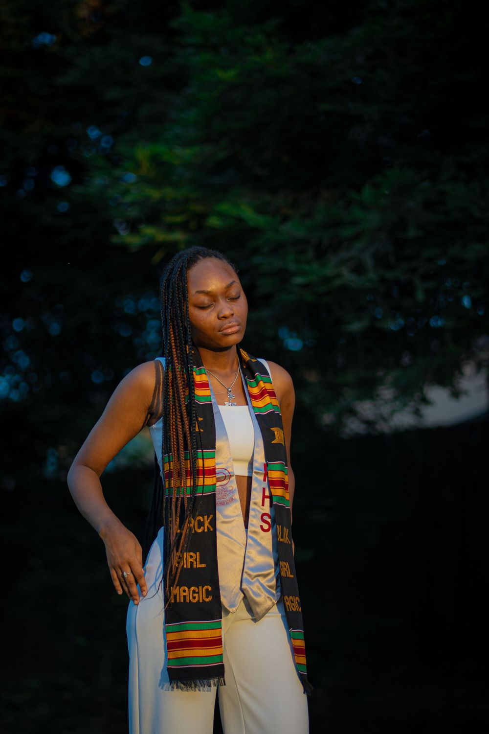 Graduate wearing traditional kente stole in artistic sunset portrait.