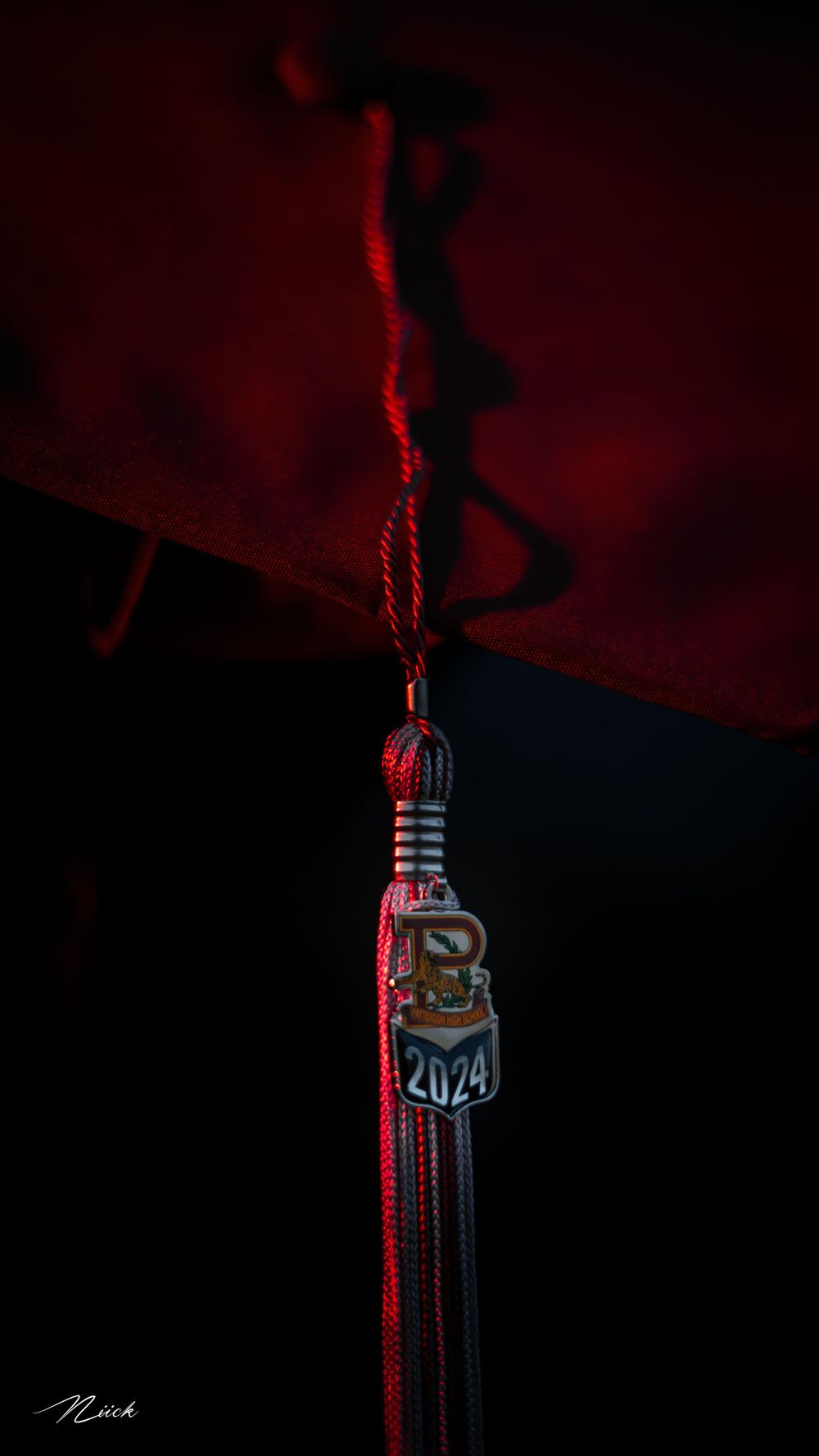 Graduation tassel with 2024 charm illuminated by dramatic red lighting.