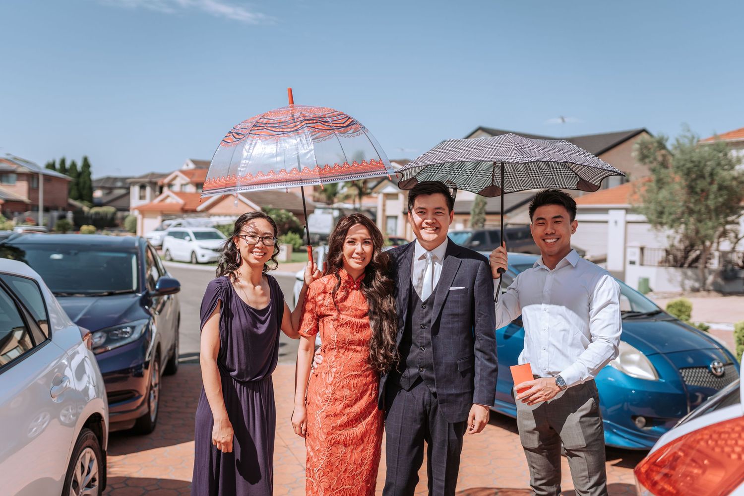 A group stands outdoors holding decorative parasols with cars and buildings visible in the background.