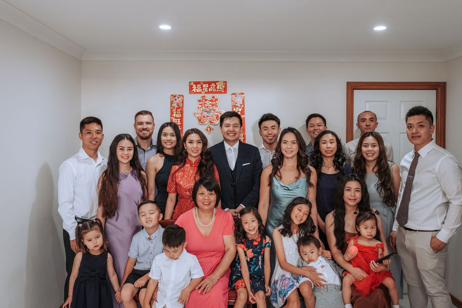 Large family group photo taken indoors with red decorations visible in the background.