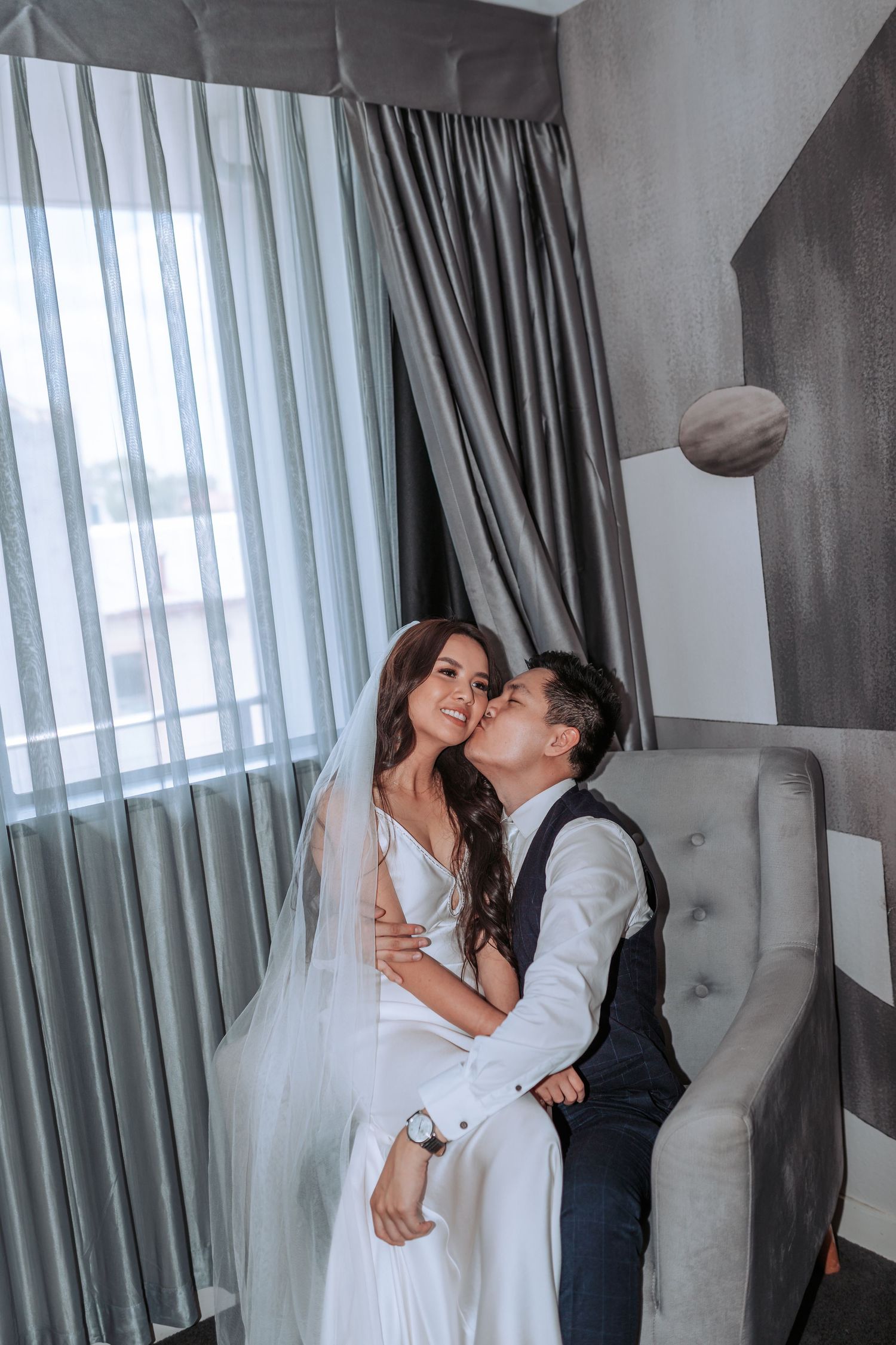A romantic wedding portrait in a modern hotel room with elegant grey curtains and a floating balloon.