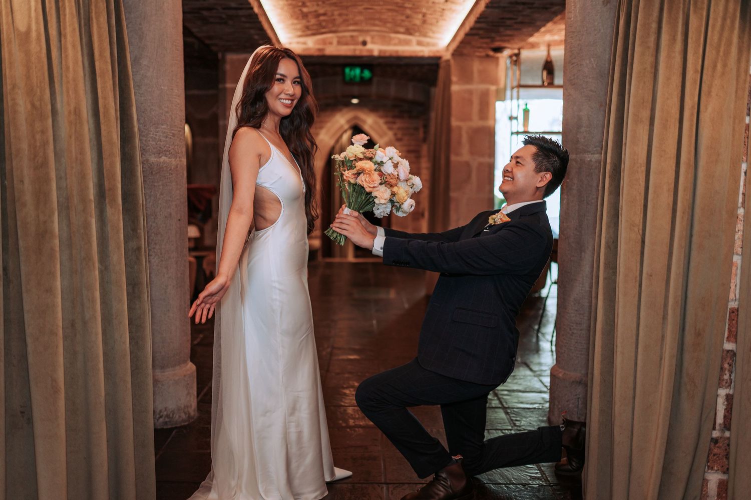 A playful wedding moment captured in a rustic wooden hallway with warm lighting.