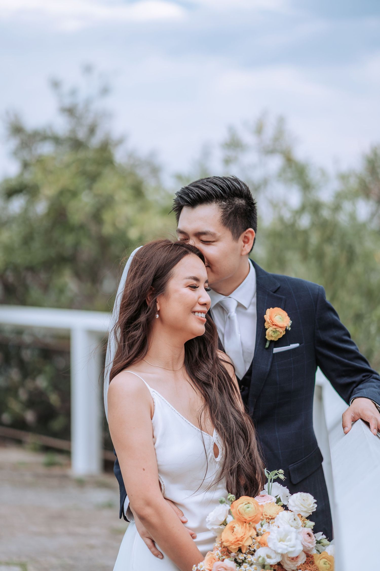 Intimate wedding moment captured outdoors with bride holding peach and white floral bouquet.