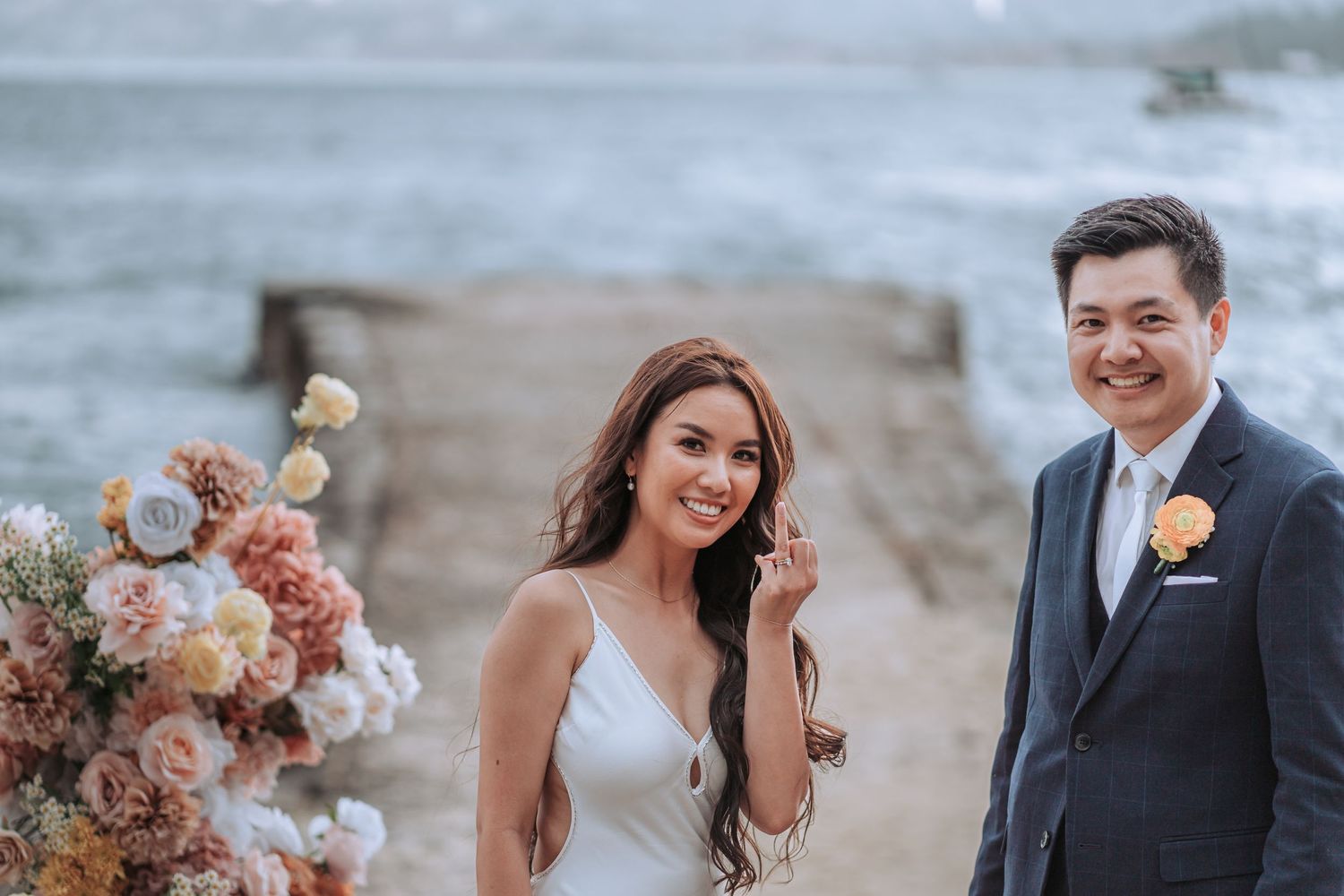 A waterfront wedding setup with peach-colored floral arrangements against an ocean backdrop.