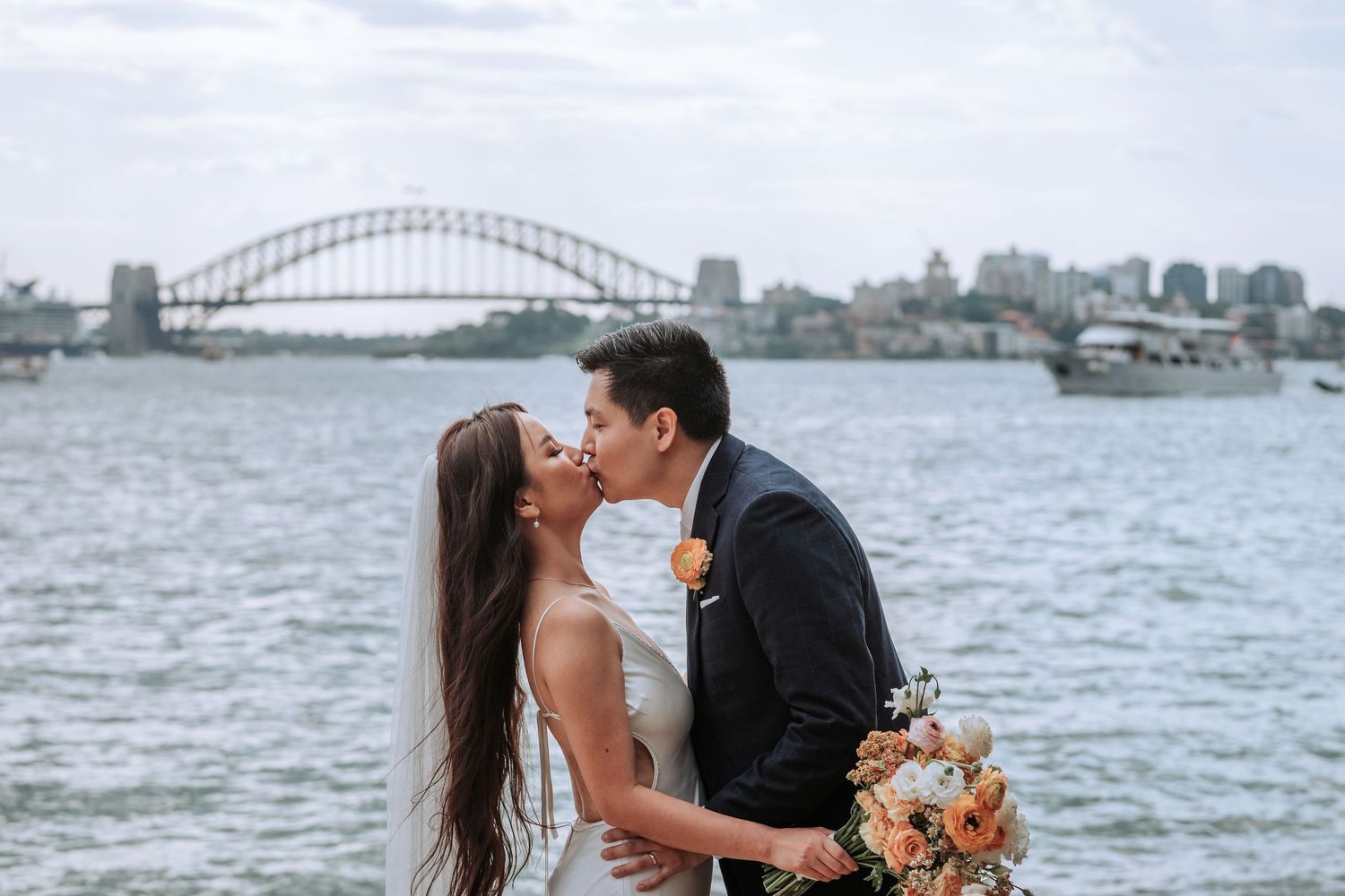 A romantic wedding moment by the water with the Sydney Harbour Bridge providing a stunning backdrop in Australia.