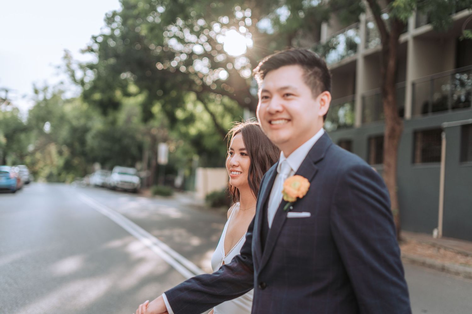 Happy wedding couple sharing a candid moment together on a tree-lined street.