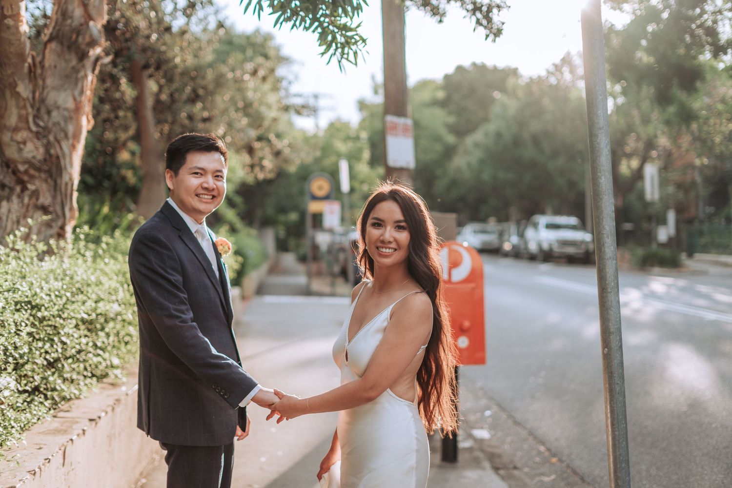 A couple shares a tender moment on a tree-lined street during their wedding photoshoot.