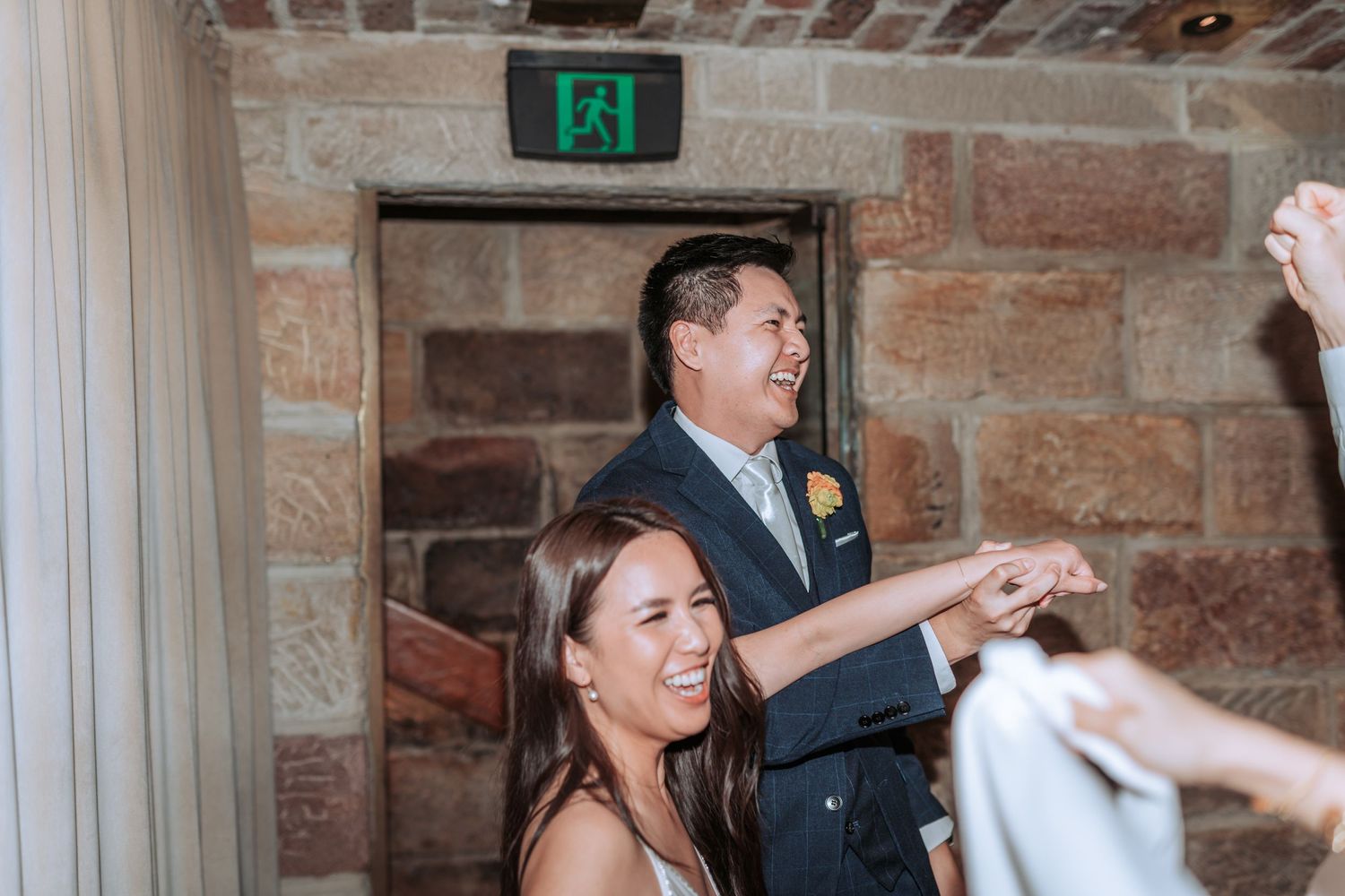 A celebratory moment in a rustic stone-walled venue with exposed brick and an exit sign overhead.