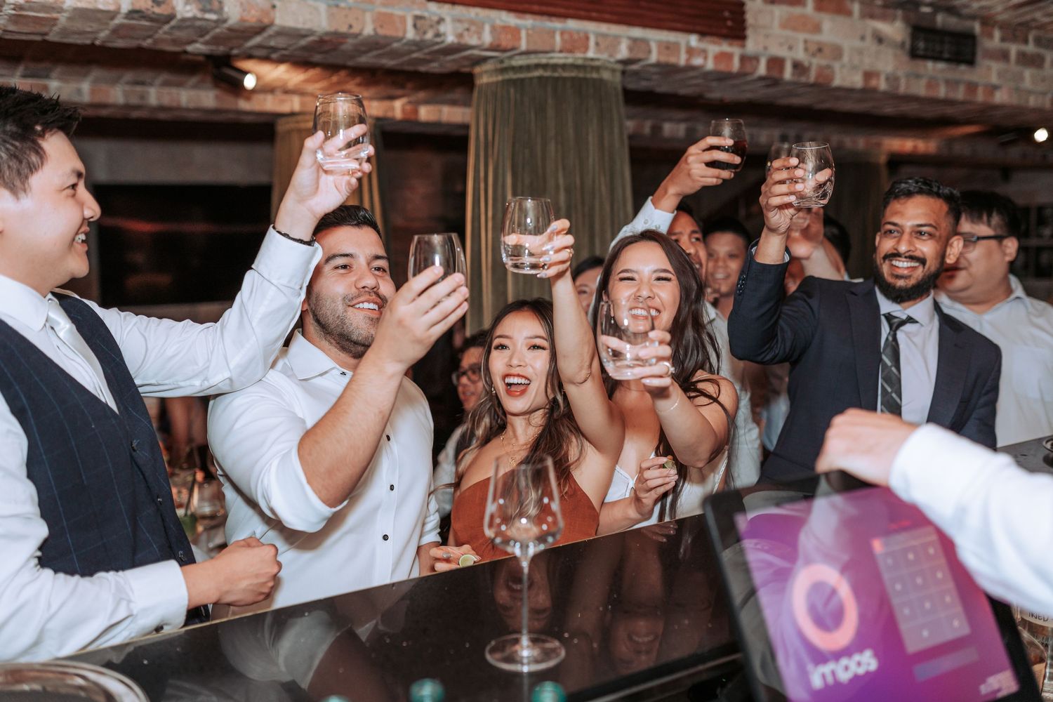 People celebrating with raised glasses at a bar counter during what appears to be a festive party event.
