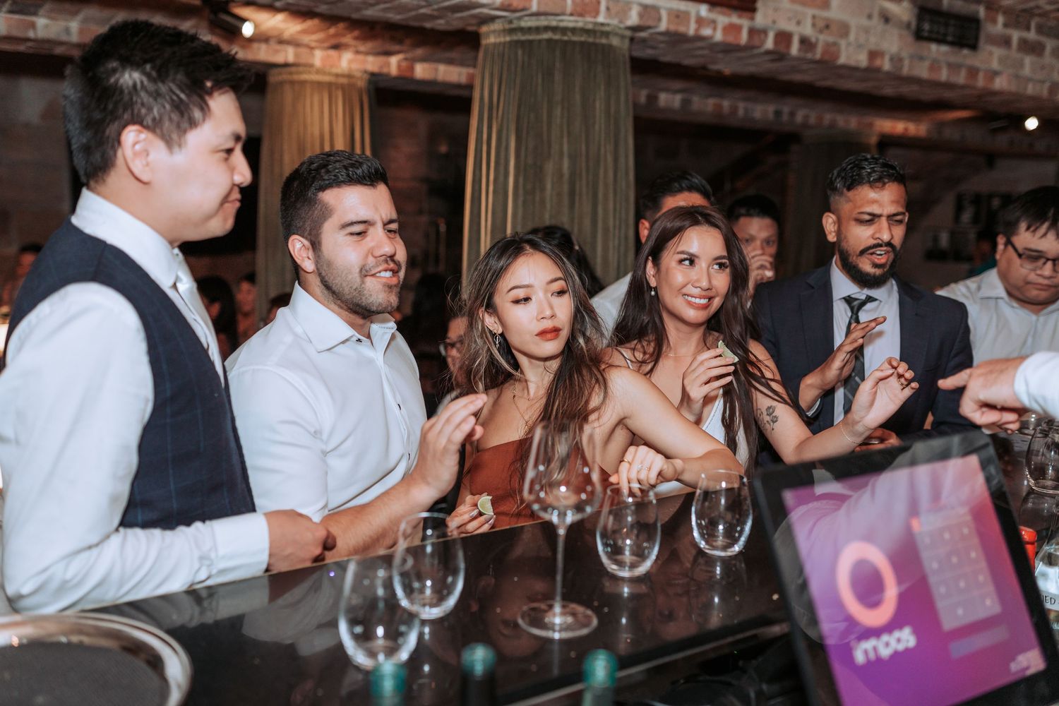 Wedding reception scene at rustic venue with guests gathered around bar area.