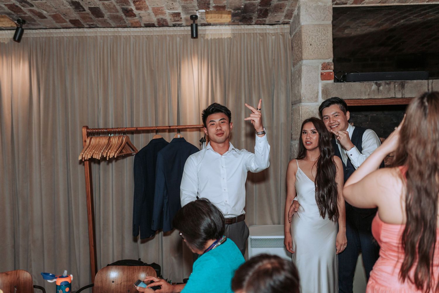 People celebrating at an indoor event space with exposed brick walls and hanging curtains.