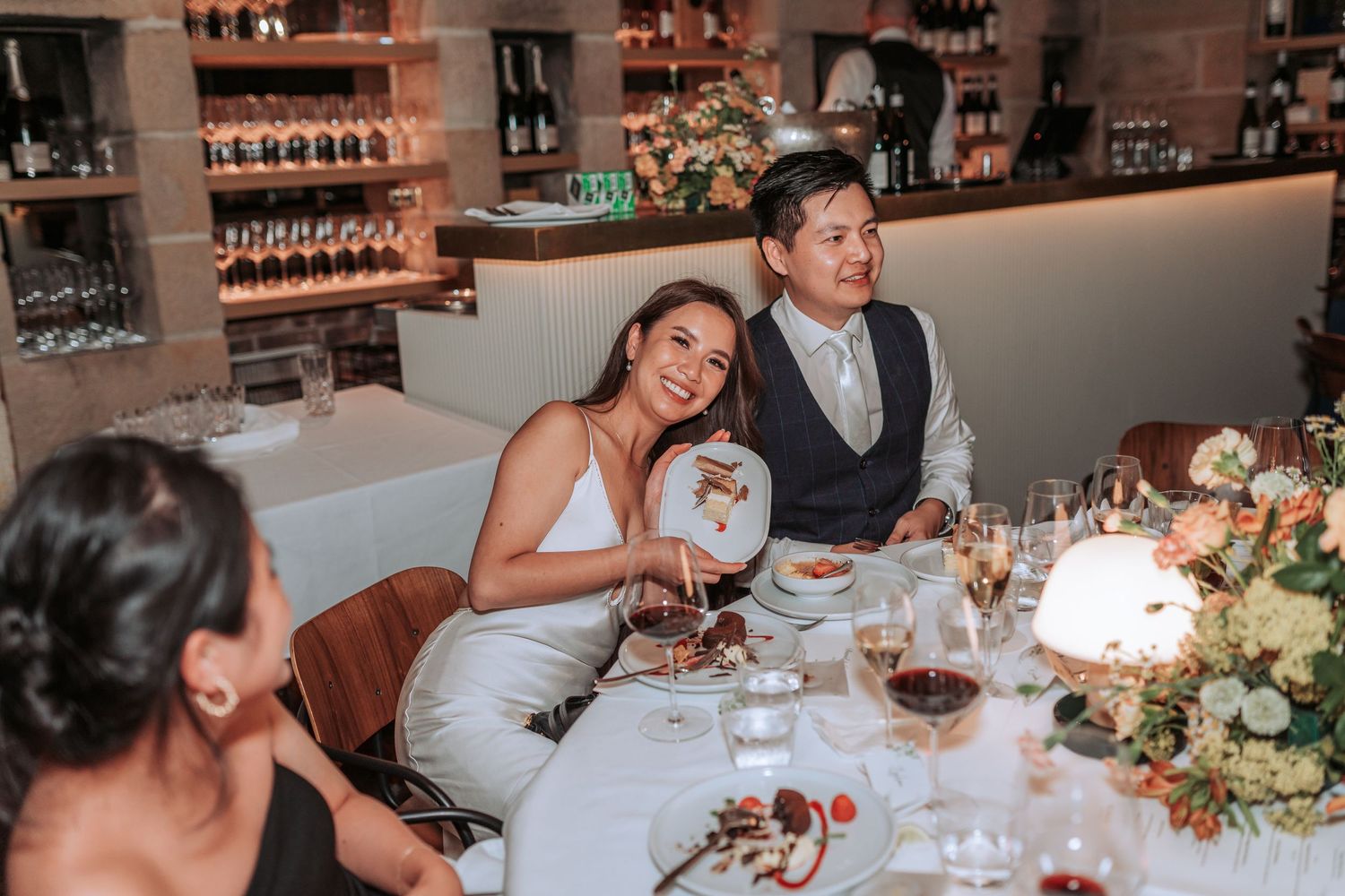 Guests enjoying an intimate wedding reception dinner at a rustic venue with wine and floral centerpieces.