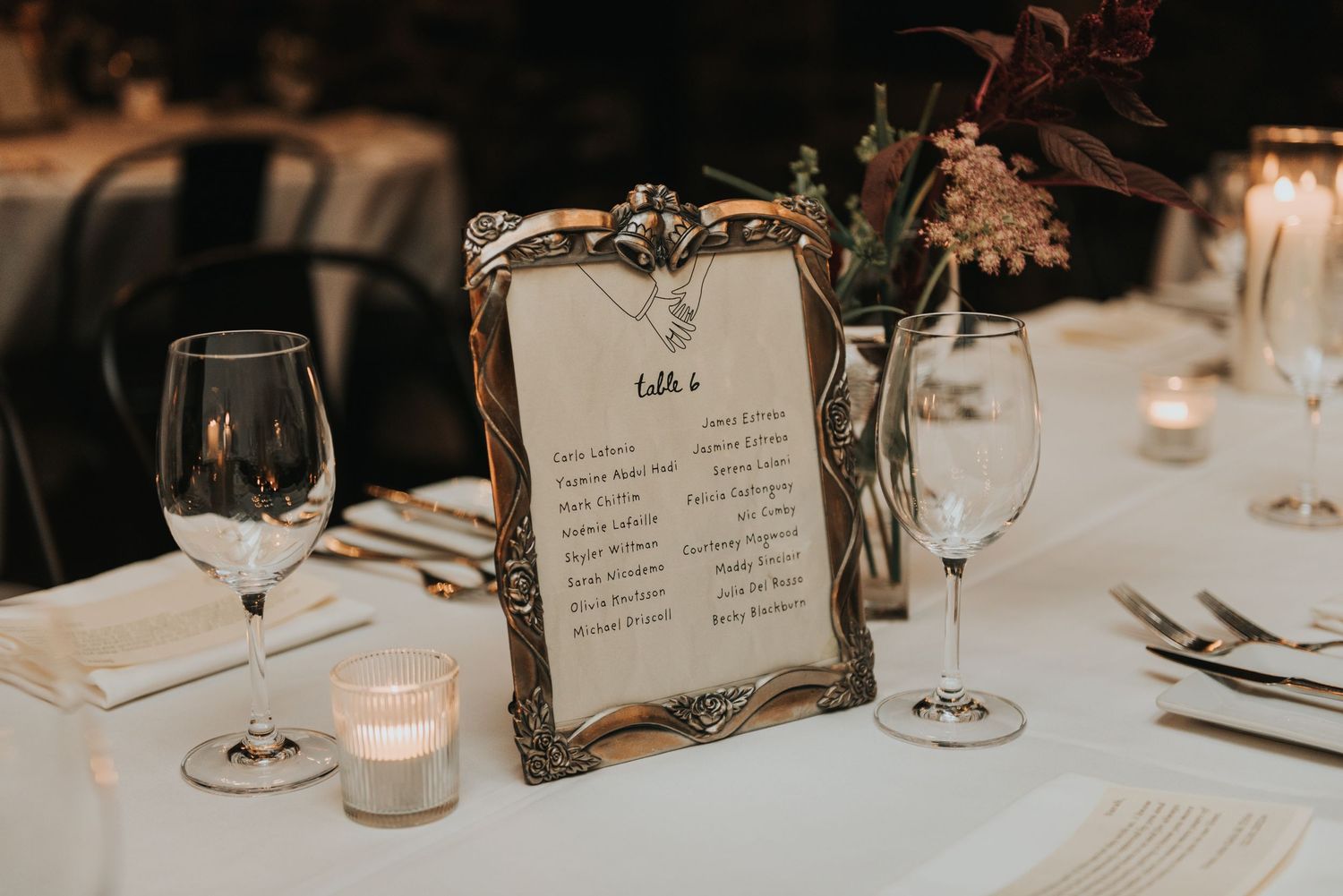 An elegant table setting at a wedding reception with framed menu card, wine glasses, and glowing candles on white linens.