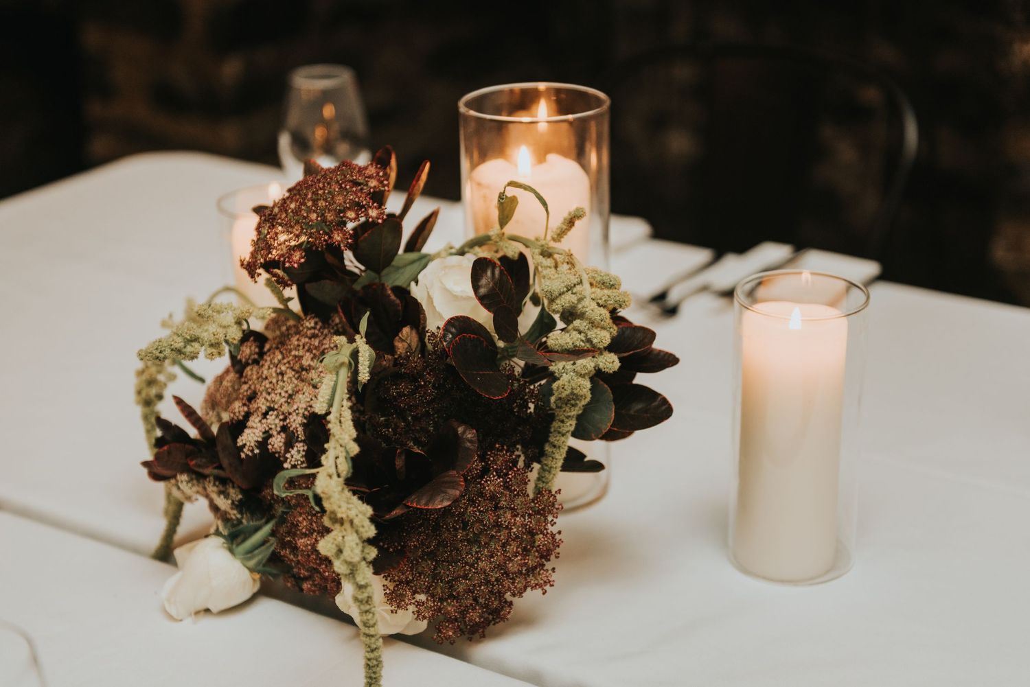 Wedding reception centerpiece with dried hydrangeas and eucalyptus alongside glowing white pillar candles on table.