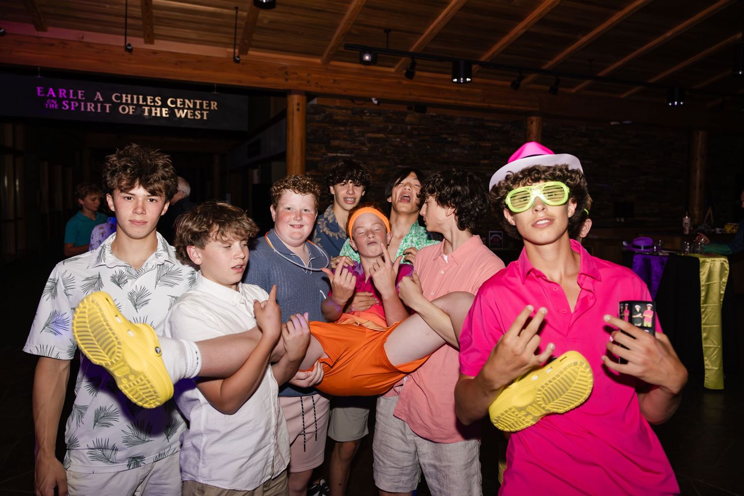 A group of friends posing together at a party with neon lighting and holding colorful inflatable objects.