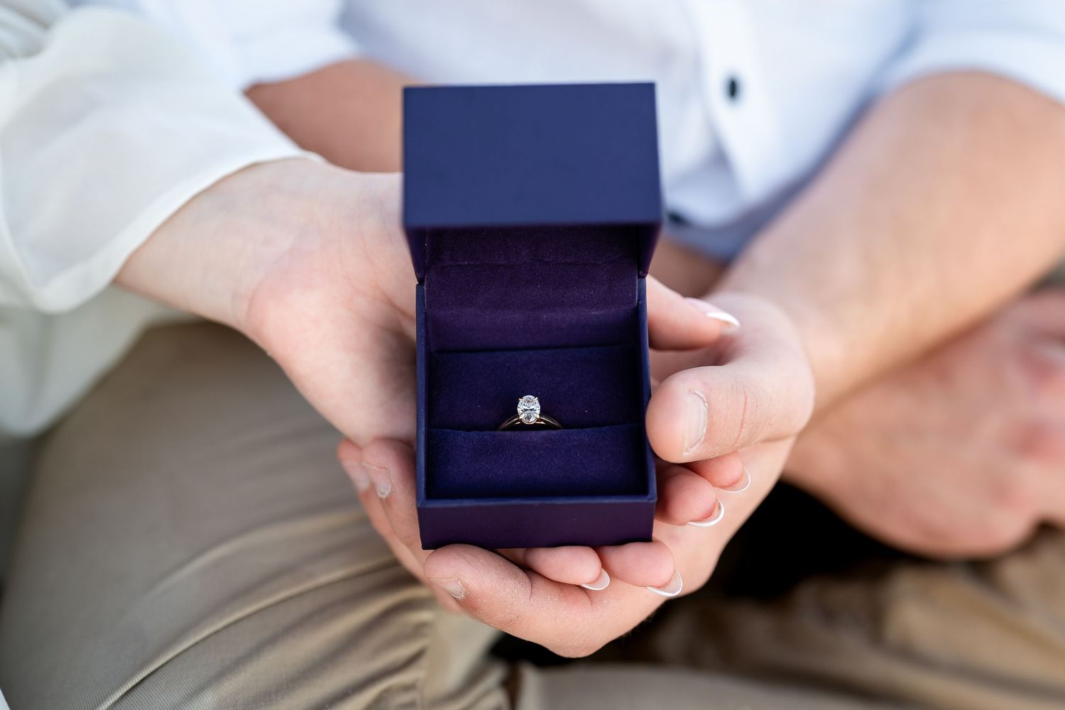 Person holding open blue velvet ring box with diamond solitaire engagement ring proposal.