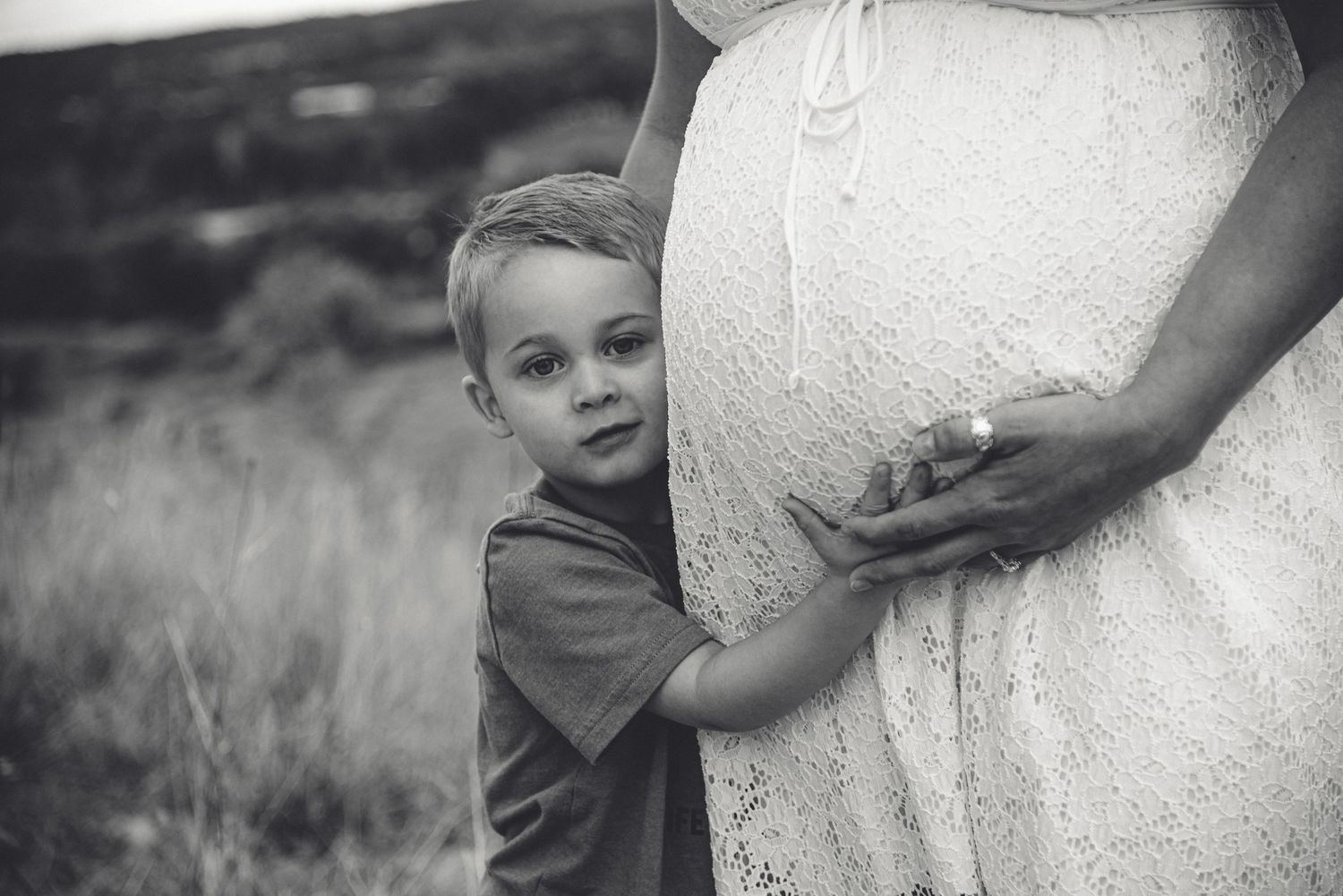 Young boy hugging a pregnant belly in a white lace dress in a black and white photo Whidbey island Maternity session