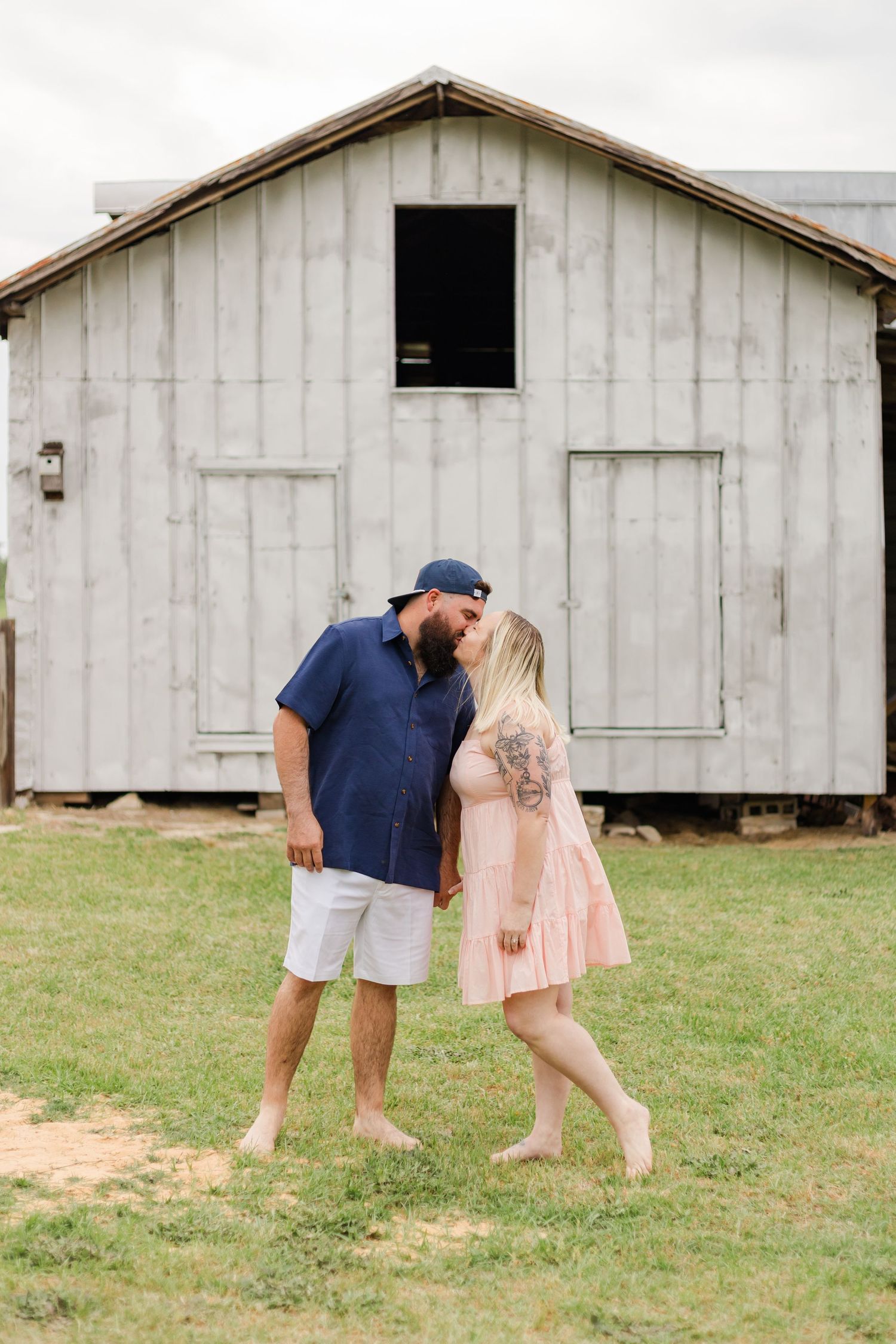 Couple in coordinated navy and pink outfits share intimate moment by rustic barn.