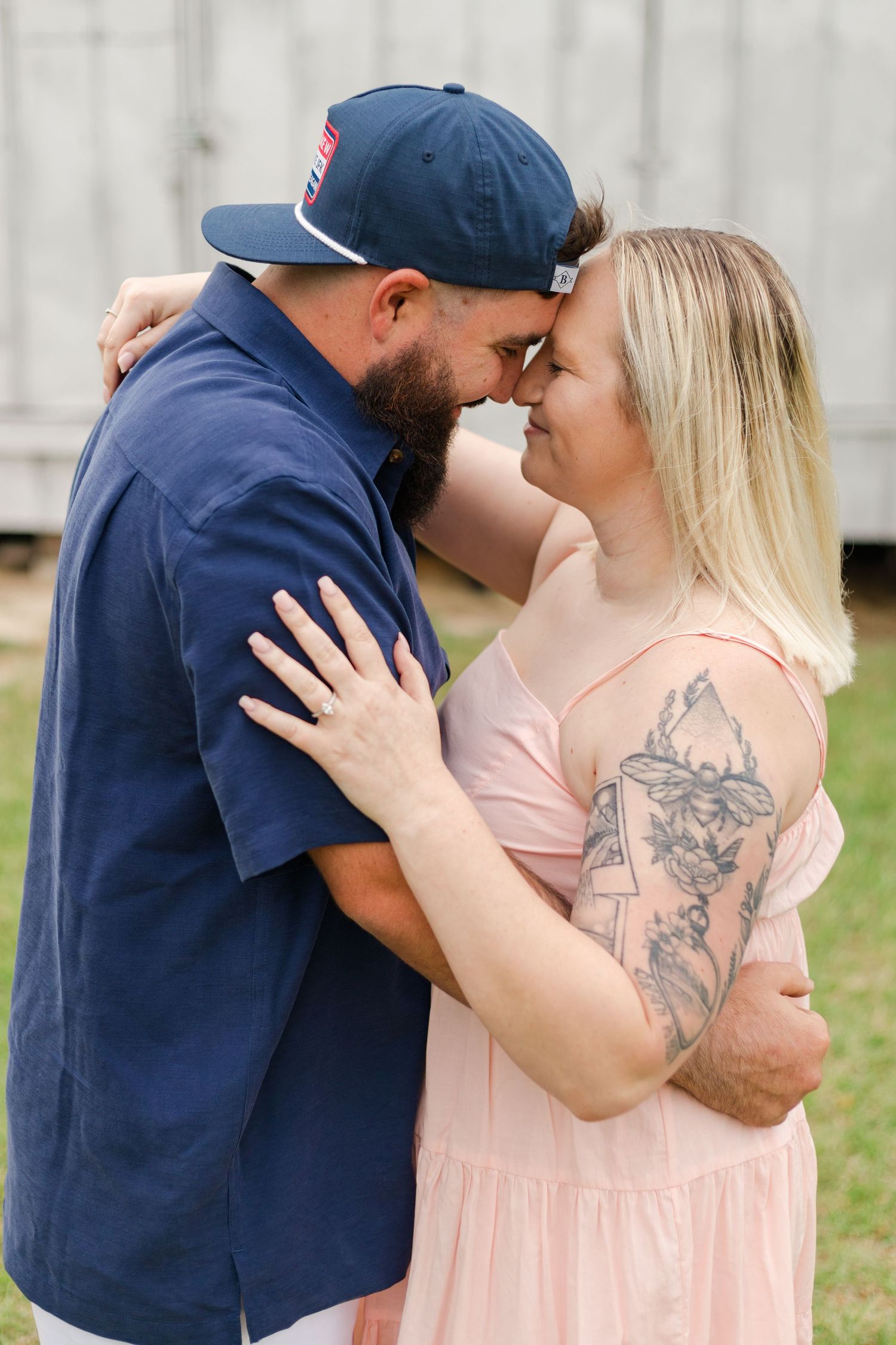 Intimate portrait of couple embracing against white barn backdrop.