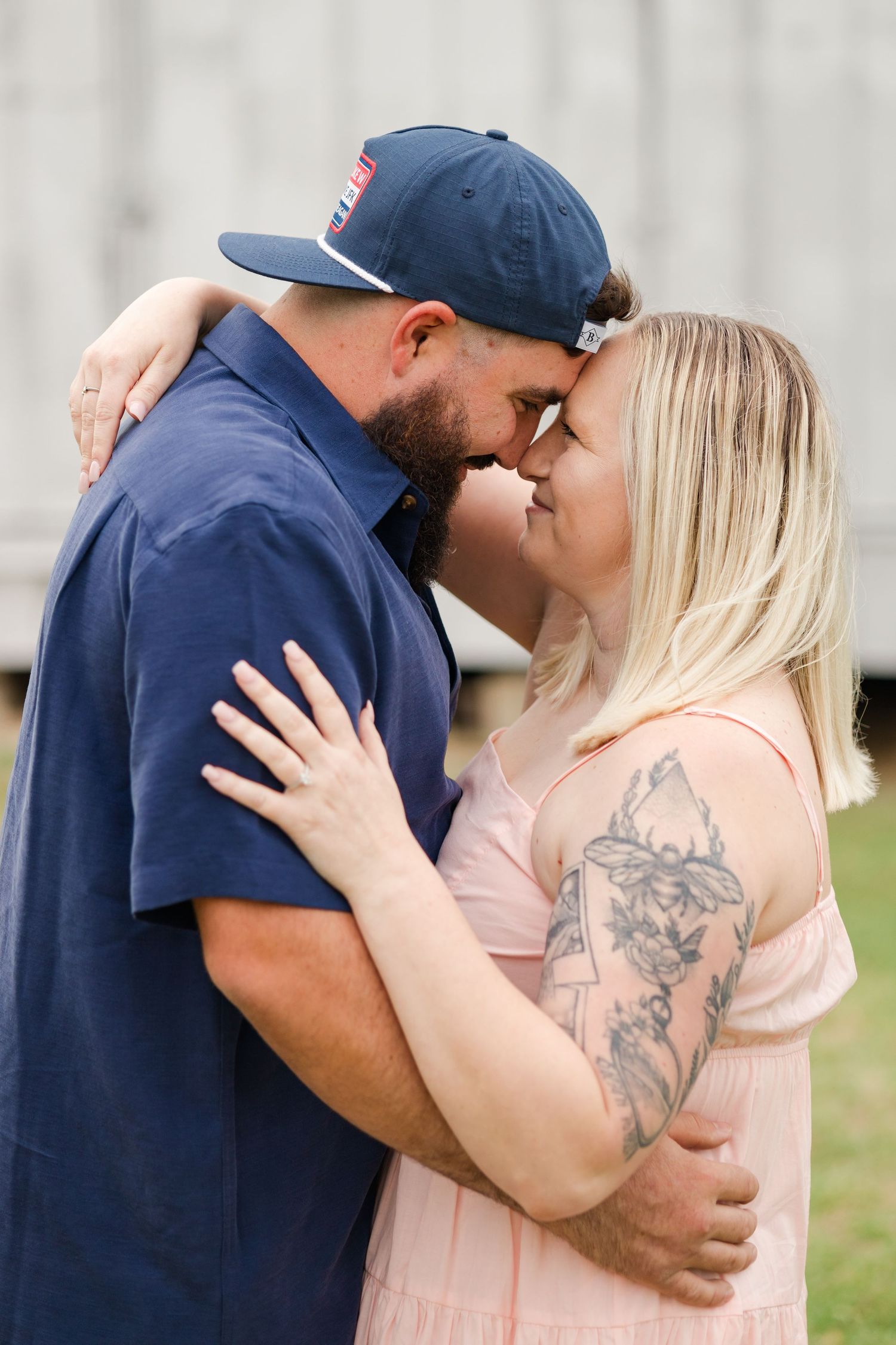 Tender moment between couple in casual attire against barn wall.