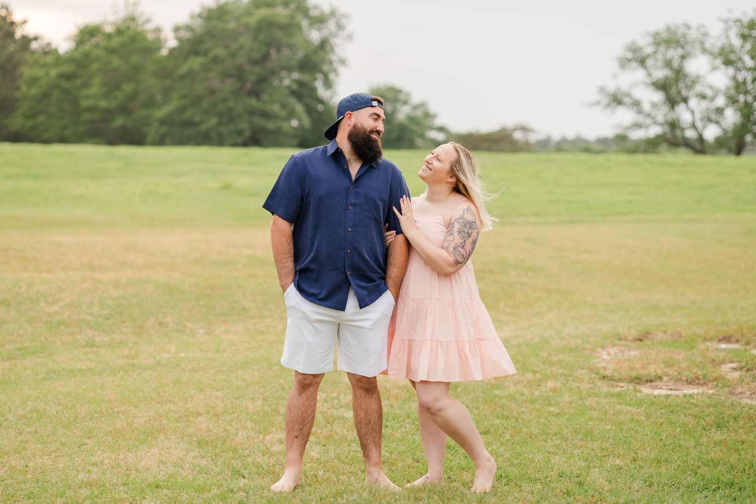 A playful outdoor photo of a couple laughing together on a green field.