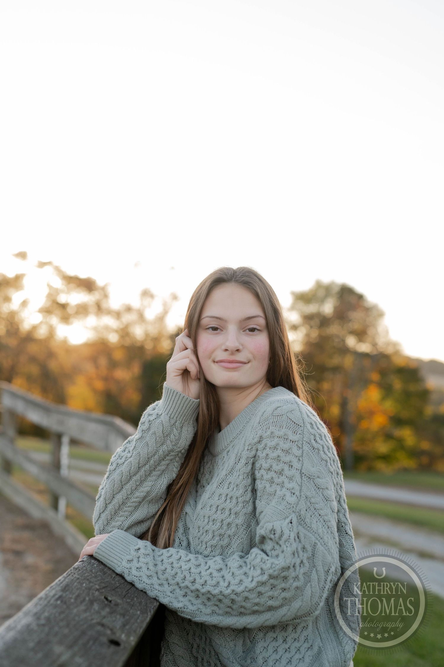 Someone in a gray sweater poses thoughtfully against an autumn sunset backdrop.
