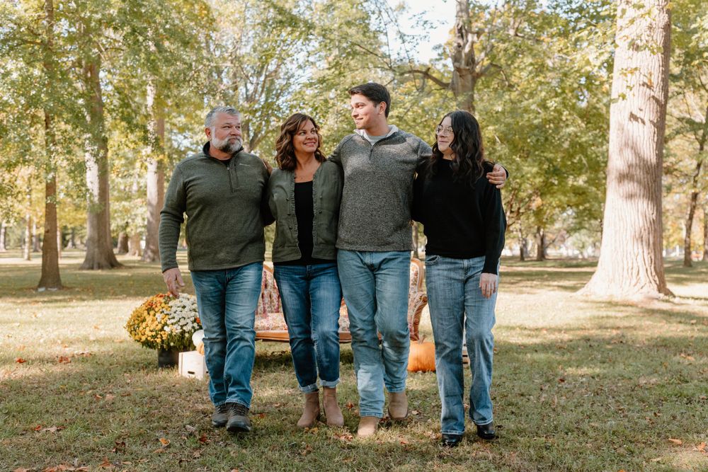 Family walking together through a park with autumn trees and fallen leaves.