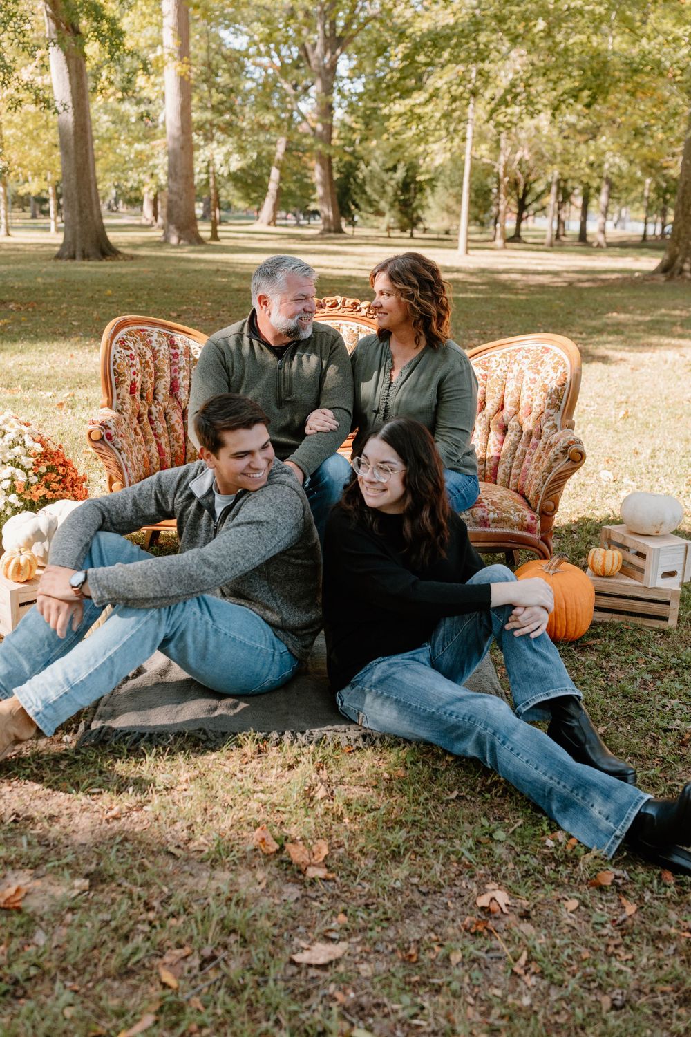 Casual outdoor family photoshoot with vintage furniture and pumpkins in autumn setting.