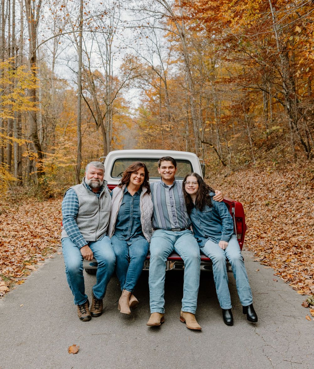Family of four in matching denim sitting on tailgate of vintage truck surrounded by fall foliage.