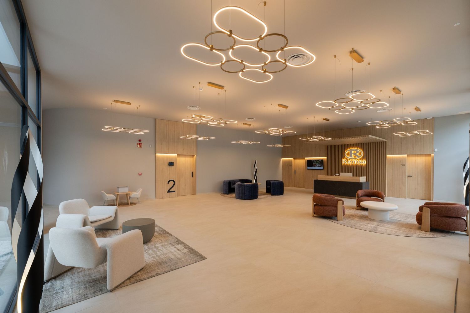 Modern hotel lobby with circular gold pendant lights, white chairs, and a sleek reception desk on polished floors.