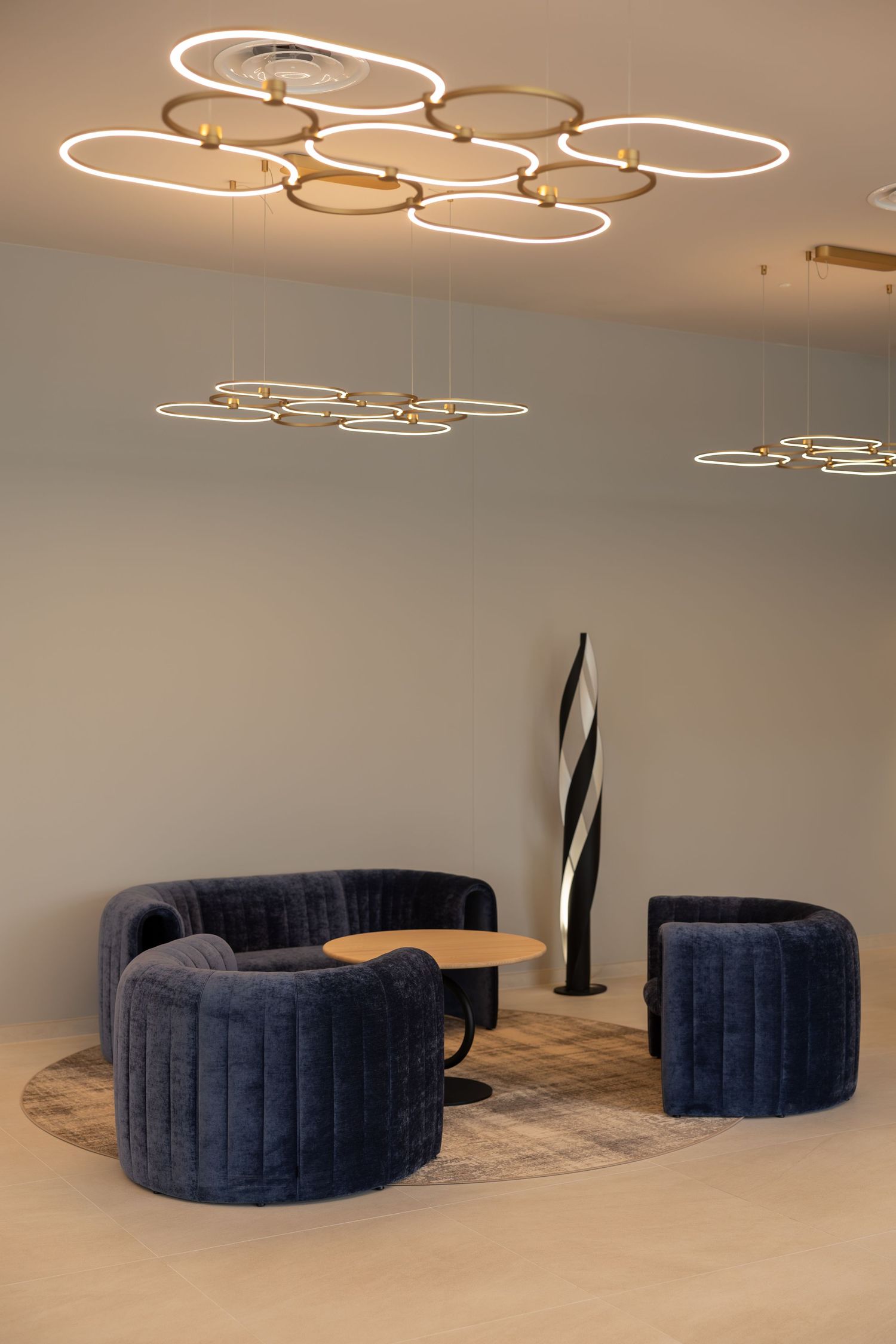 Modern lounge with navy velvet curved sofas, round coffee table, and elegant circular gold pendant lights on beige ceiling.