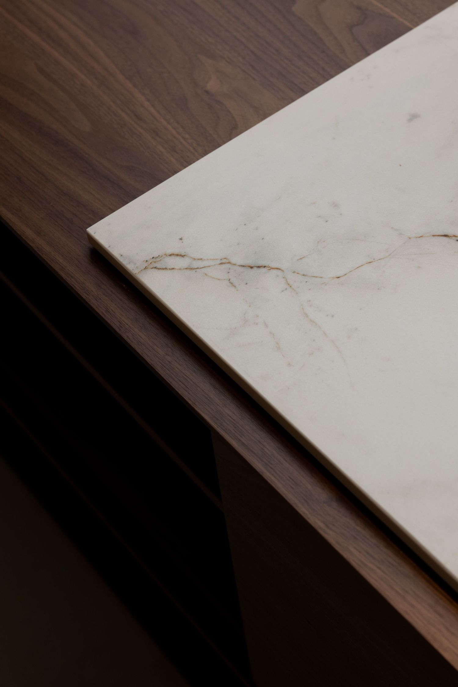 Close-up of a white marble tabletop with gold veining resting on a dark walnut wood base.