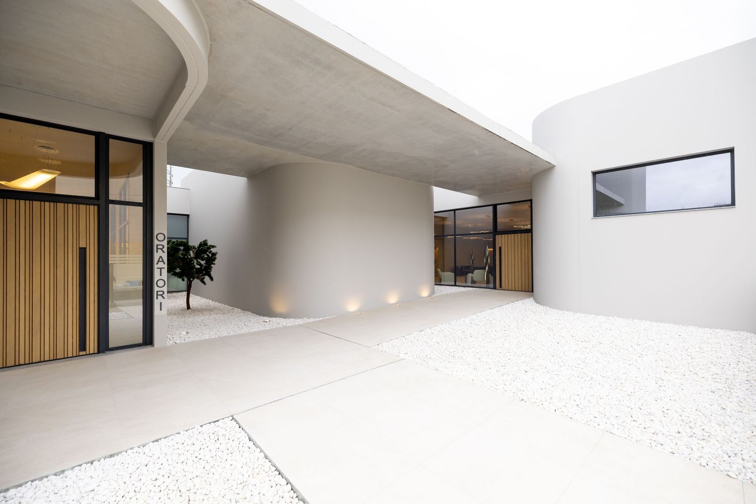 Modern minimalist courtyard with curved concrete canopy, gravel ground, and floor lighting at a contemporary architectural home.