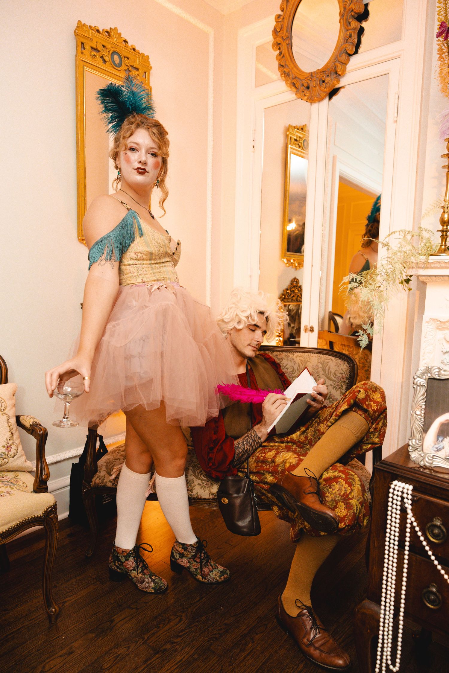 Two women in vintage-inspired costumes pose in an elegantly decorated room during a themed party event.