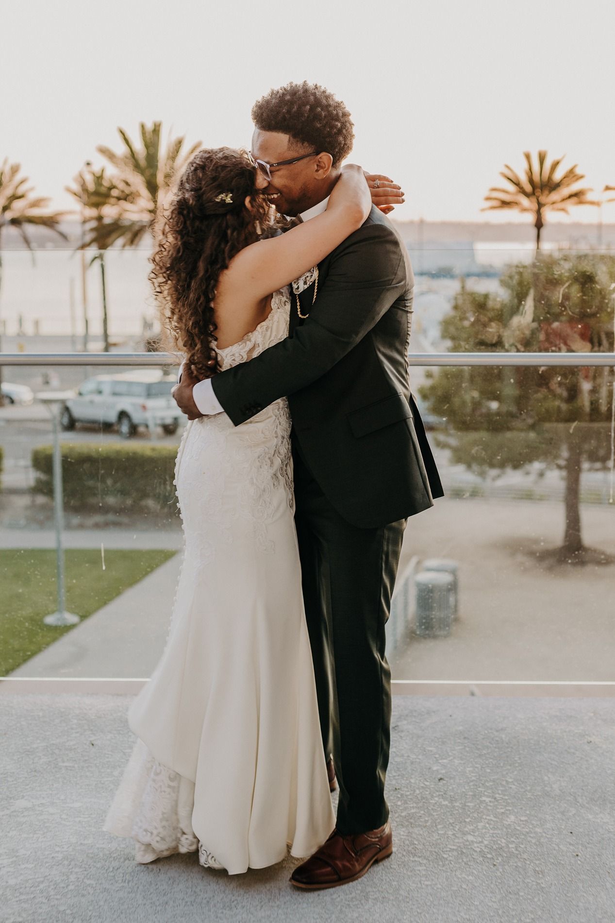 A bride and groom share a romantic embrace on an outdoor balcony with palm trees in the background at The Lane.