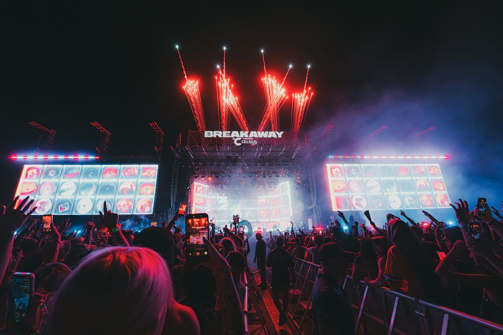 Breakaway Music Festival crowd cheering under red fireworks with vibrant LED stage displays at night.