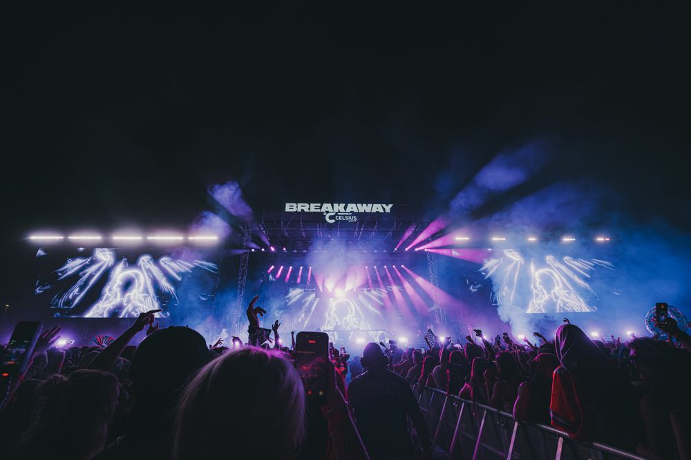 Breakaway Music Festival crowd cheering under vibrant blue and purple stage lights at an outdoor night concert.