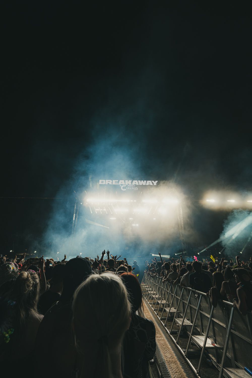 Crowd at Breakaway Music Festival at night with bright stage lights and smoke filling the dark sky.