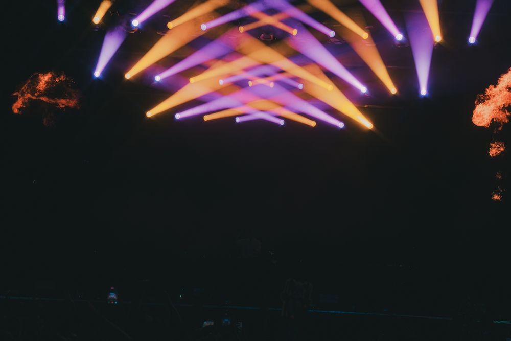 Colorful purple and yellow stage lights illuminating an outdoor concert venue at night.