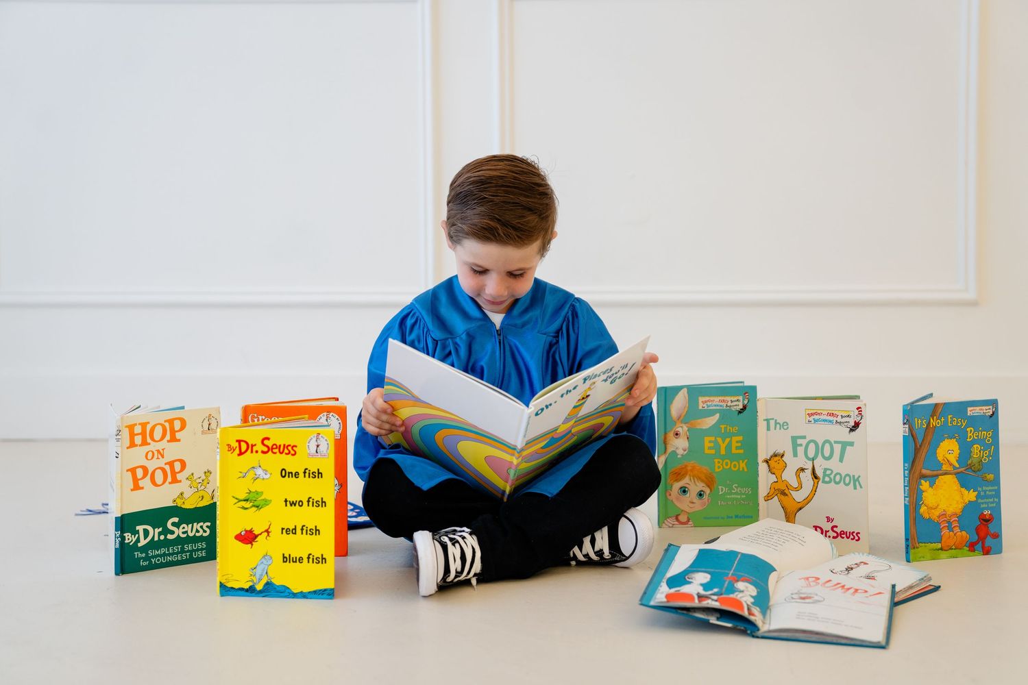 Young boy sitting cross-legged on floor reading Dr. Seuss books surrounded by colorful titles like Hop on Pop.