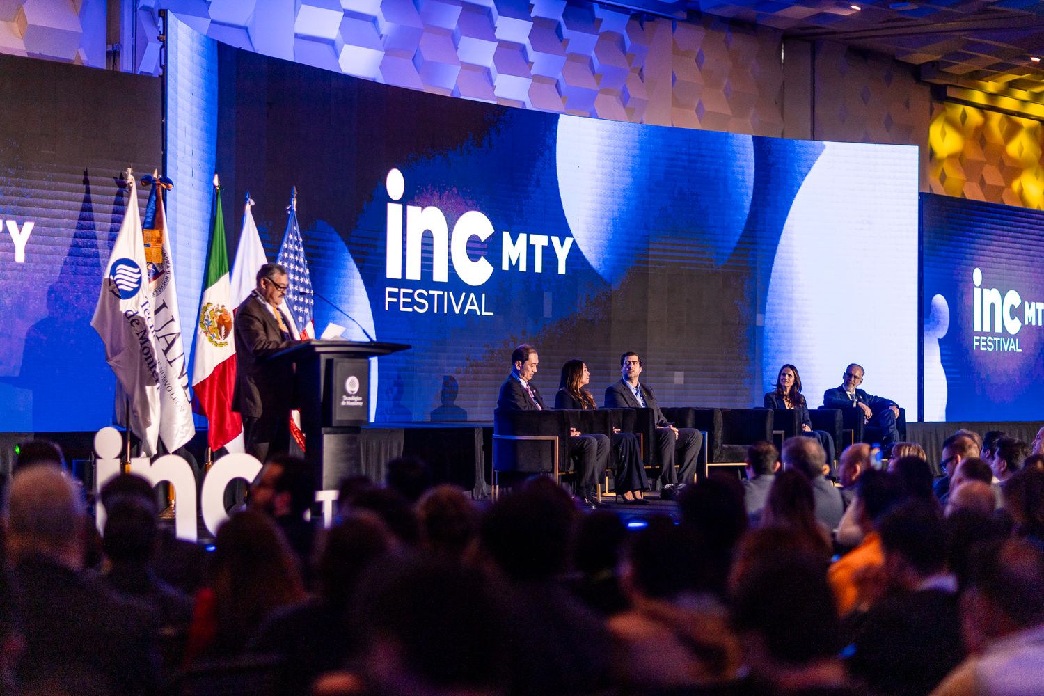 Group of professionals on stage at an organized event, standing under a blue backdrop with text.