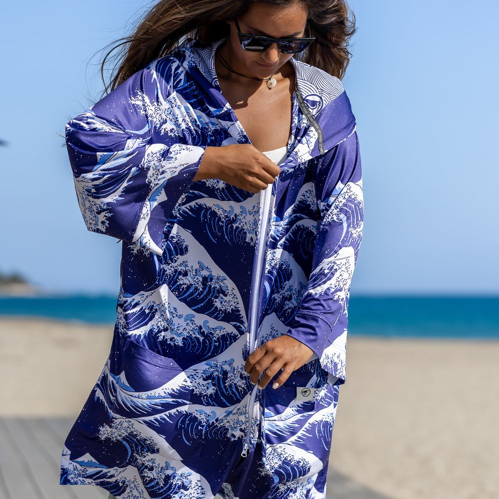Woman wearing a blue and white Japanese wave print zip-up jacket on a sunny beach.
