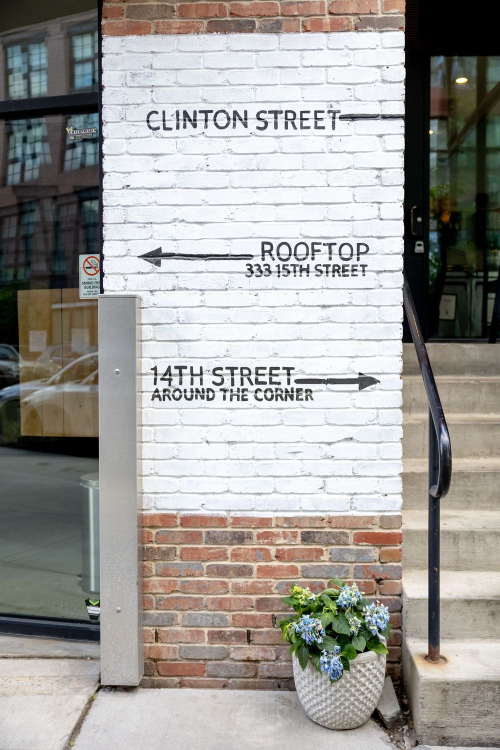 White painted brick wall with directional signs for Clinton Street, Rooftop at 333 15th Street, and 14th Street around the corner.
