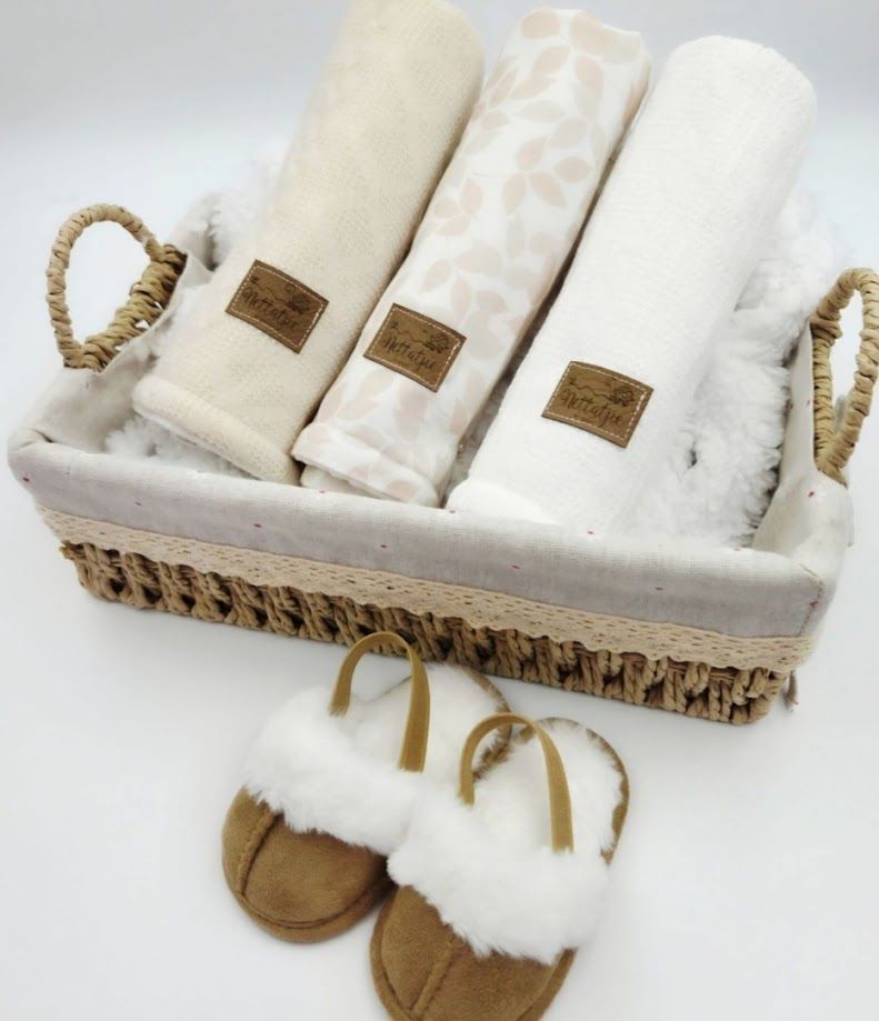 Wicker basket with cream folded blankets and plush fur-trimmed sandals, perfect for a cozy gift set.