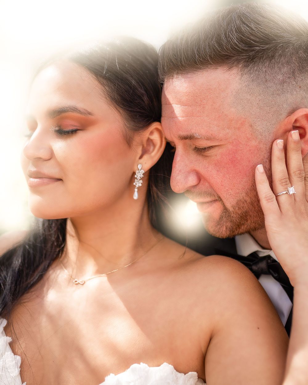 Bride and groom share an intimate wedding moment, bride wearing crystal drop earrings and diamond ring.