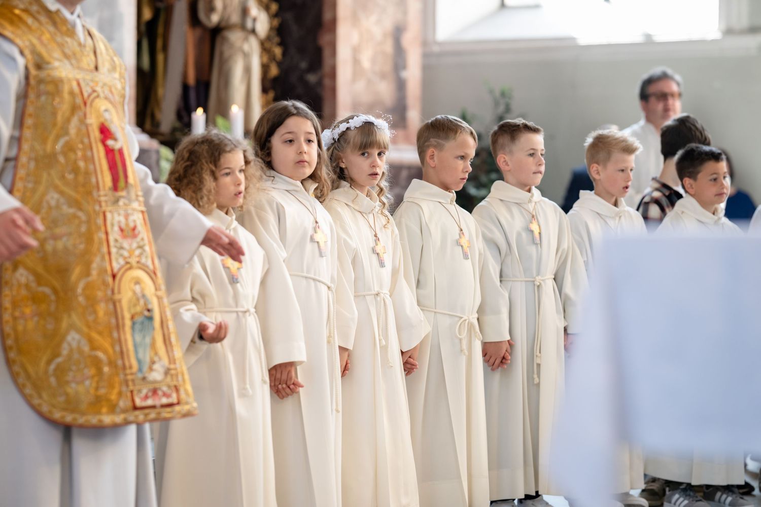 Kommunionkinder in weißen Gewändern stehen mit dem Priester in der Kirche