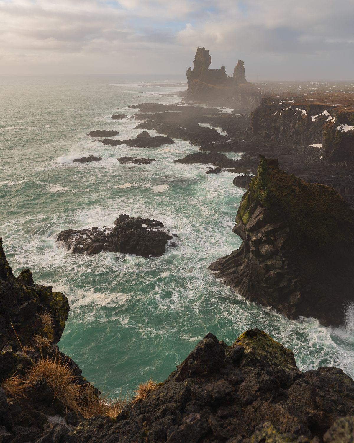 Dramatic rocky coastline with jagged sea stacks rising from turbulent green ocean waves in Iceland.